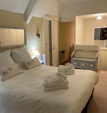 Suite La Tour : grand lit blanc, serviettes pliées et poutres apparentes